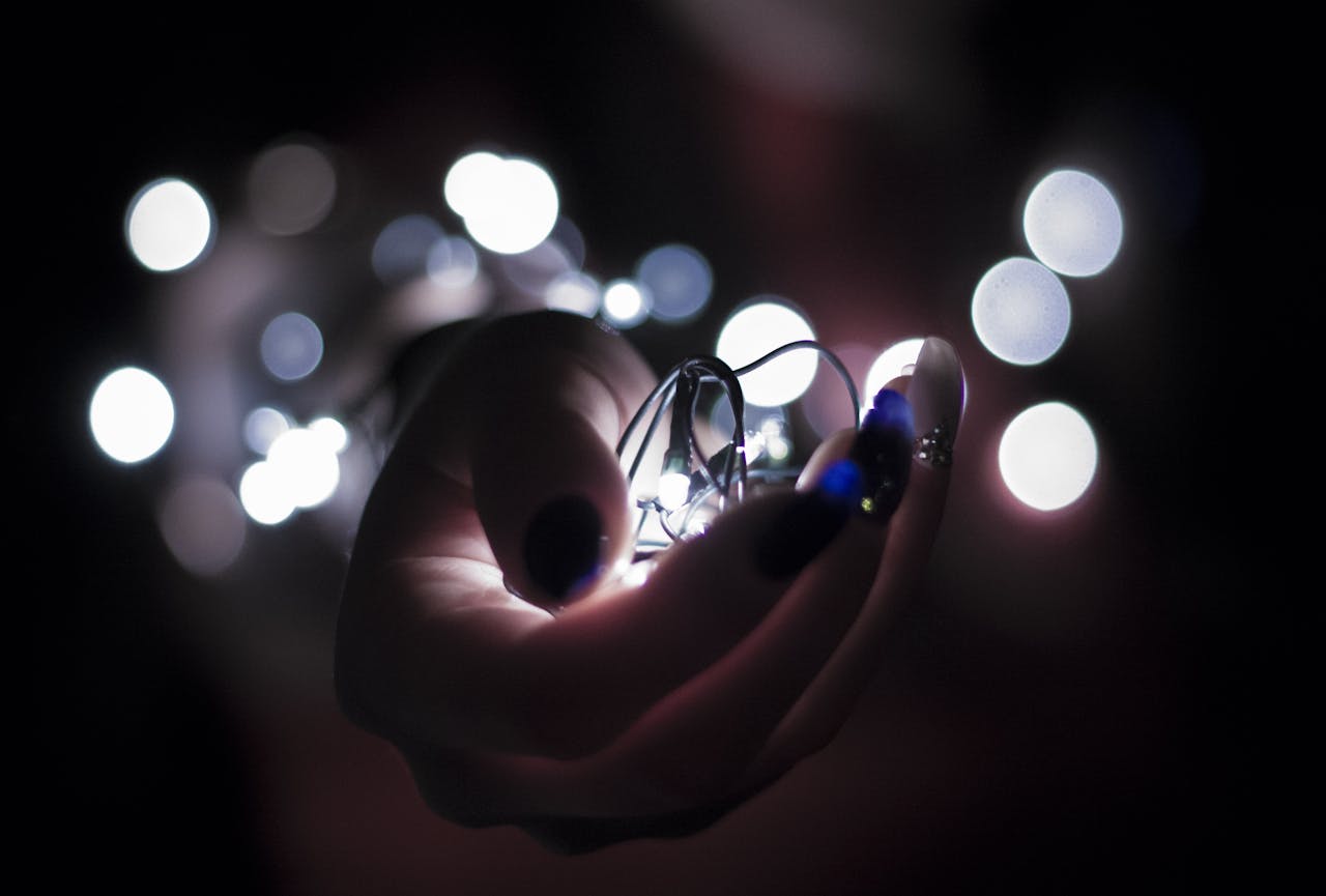 Close-up of a hand holding glowing string lights with a bokeh effect, creating a festive atmosphere.